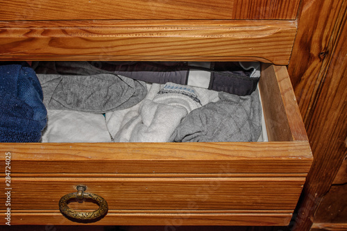 Open retractable drawer of an old wooden cabinet with clothes