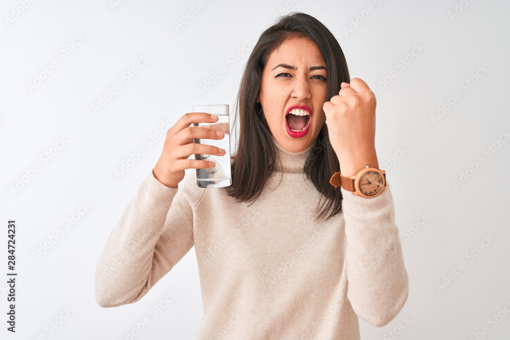 Young beautiful chinese woman holding glass of water standing over isolated white background annoyed and frustrated shouting with anger, crazy and yelling with raised hand, anger concept Young beautiful chinese woman holding glass of water standing over isolated white background annoyed and frustrated shouting with anger, crazy and yelling with raised hand, anger concept