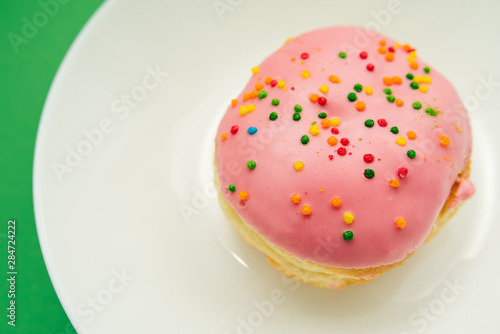 Pink round donut on white plate on green background