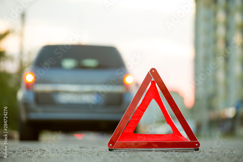 Red emergency triangle stop sign and broken car on a city street.