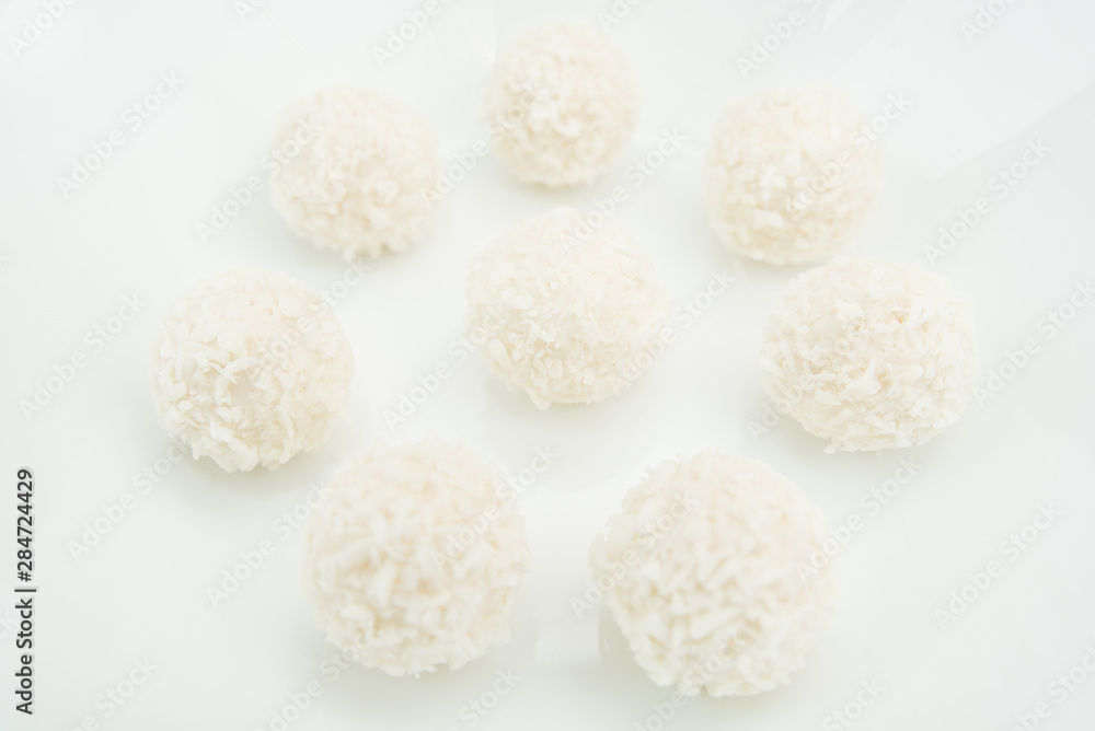 Chocolate covered coconut candies on white plate isolated on black background. Truffle candy set. Selective focus