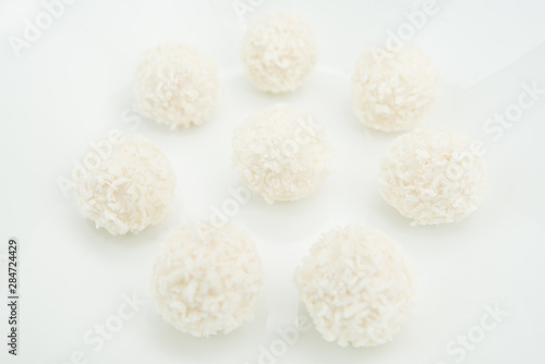 Chocolate covered coconut candies on white plate isolated on black background. Truffle candy set. Selective focus