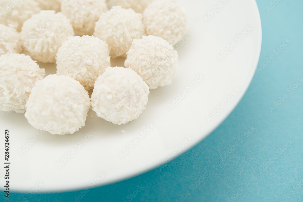 Chocolate covered coconut candies on white plate isolated on blue background. Truffle candy set. Selective focus