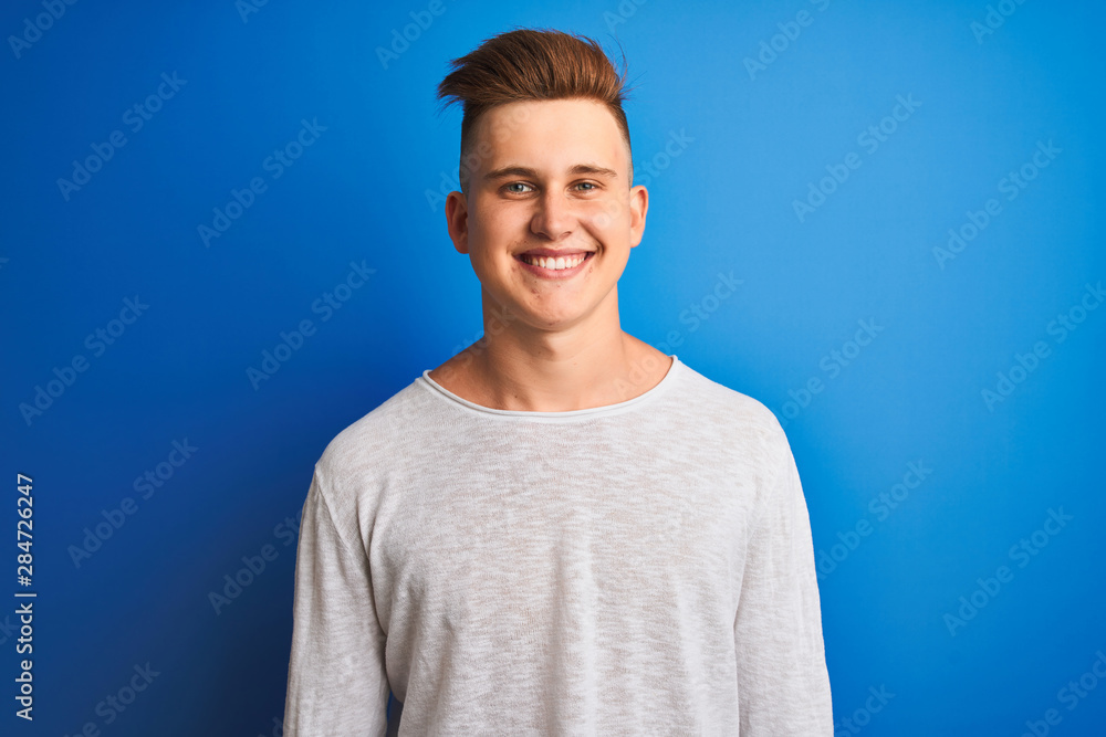 Young handsome man wearing white casual t-shirt standing over isolated blue background with a happy face standing and smiling with a confident smile showing teeth Young handsome man wearing white casual t-shirt standing over isolated blue background with a happy face standing and smiling with a confident smile showing teeth