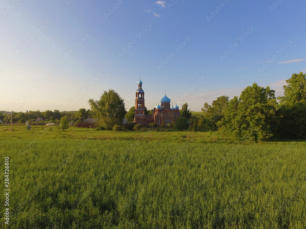 Green grass, blue sky, and a Church of our lady mother of Kazan in Smolyarova in the distance. Tatarstan, Russia