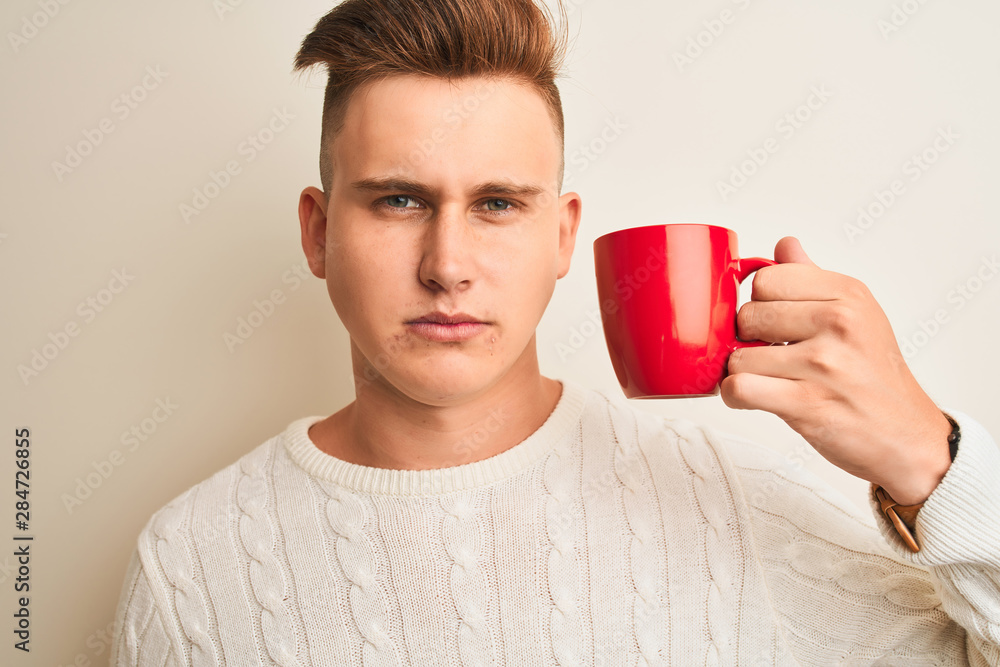 Young handsome man drinking red cup of coffee standing over isolated white background with a confident expression on smart face thinking serious Young handsome man drinking red cup of coffee standing over isolated white background with a confident expression on smart face thinking serious
