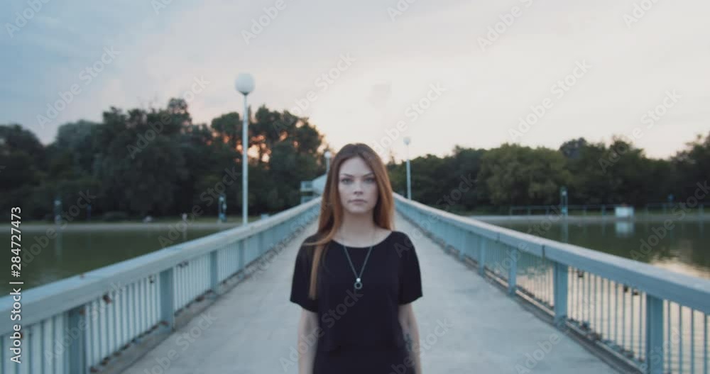 Young woman with nose piercing dressed in black walks toward the camera on a bridge in slow motion Young woman with nose piercing dressed in black walks toward the camera on a bridge in slow motion