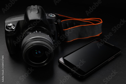 Professional digital slr camera and smartphone on black background