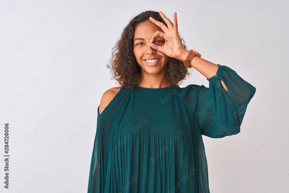 Young brazilian woman wearing green t-shirt standing over isolated white background doing ok gesture with hand smiling, eye looking through fingers with happy face. Young brazilian woman wearing green t-shirt standing over isolated white background doing ok gesture with hand smiling, eye looking through fingers with happy face.