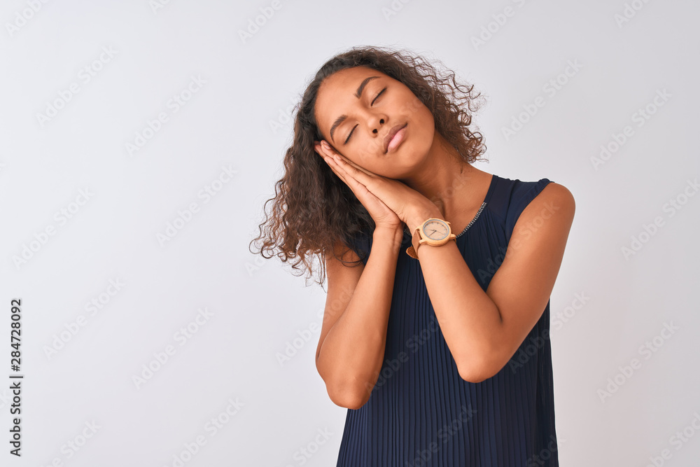 Young brazilian woman wearing blue dress standing over isolated white background sleeping tired dreaming and posing with hands together while smiling with closed eyes. Young brazilian woman wearing blue dress standing over isolated white background sleeping tired dreaming and posing with hands together while smiling with closed eyes.