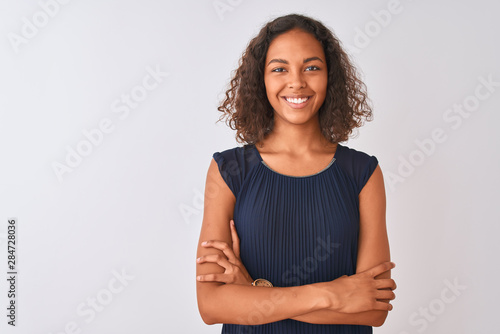 Young brazilian woman wearing blue dress standing over isolated white background happy face smiling with crossed arms looking at the camera. Positive person.