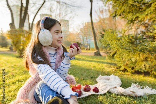 Child girl eating fresh red apples in sunny autumn park