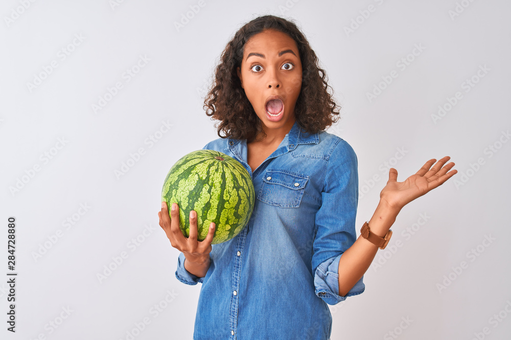 Young brazilian woman holding watermelon standing over isolated white background very happy and excited, winner expression celebrating victory screaming with big smile and raised hands Young brazilian woman holding watermelon standing over isolated white background very happy and excited, winner expression celebrating victory screaming with big smile and raised hands