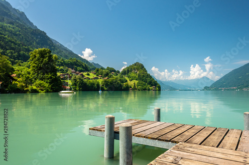 View of Brienz lake with clear turquoise water. Wooden pier. Traditional wooden houses on the shore of Brienz lake in the village of Iseltwald, Switzerland photo