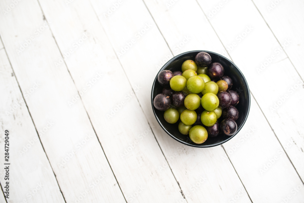 Muscadine grapes are also known as swamp grapes, Florida grapes in a bowl on wood background Muscadine grapes are also known as swamp grapes, Florida grapes in a bowl on wood background