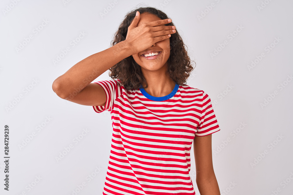 Young brazilian woman wearing red striped t-shirt standing over isolated white background smiling and laughing with hand on face covering eyes for surprise. Blind concept. Young brazilian woman wearing red striped t-shirt standing over isolated white background smiling and laughing with hand on face covering eyes for surprise. Blind concept.