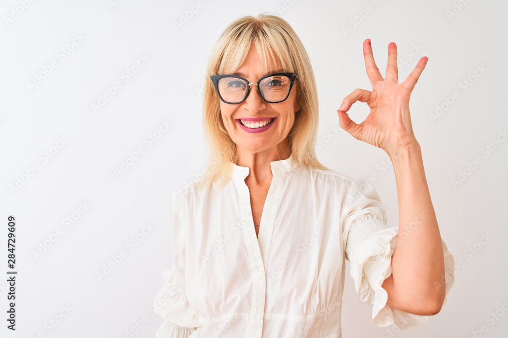 Middle age businesswoman wearing shirt and glasses standing over isolated white background doing ok sign with fingers, excellent symbol Middle age businesswoman wearing shirt and glasses standing over isolated white background doing ok sign with fingers, excellent symbol