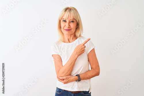 Middle age woman wearing casual t-shirt standing over isolated white background Pointing with hand finger to the side showing advertisement, serious and calm face