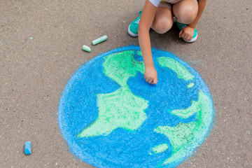 the  child girl draws a planet of the world with colored chalk on the asphalt. Children's drawings, paintings and concepts. Education and art, be creative when you return to school.  earth, Peace day