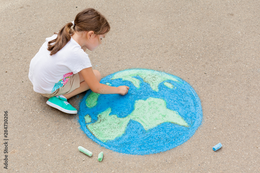Φωτογραφία the  child girl draws a planet of the world with colored chalk on the asphalt