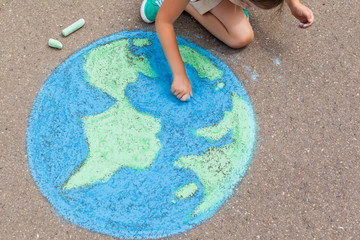 the  child girl draws a planet of the world with colored chalk on the asphalt. Children's drawings, paintings and concepts. Education and art, be creative when you return to school.  earth, Peace day