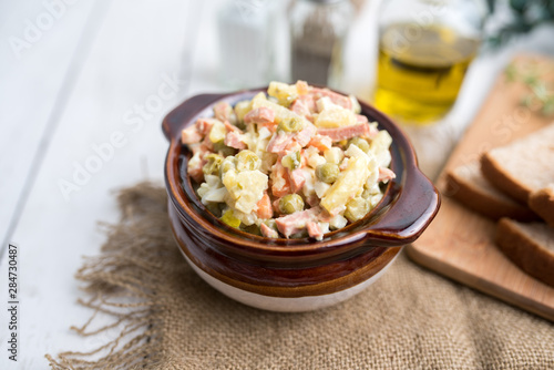 Bowl of traditional Russian salad called Olivie, Russian New Year or Christmas salad on wooden background. Salad from cooked vegetables. Potato salad. 