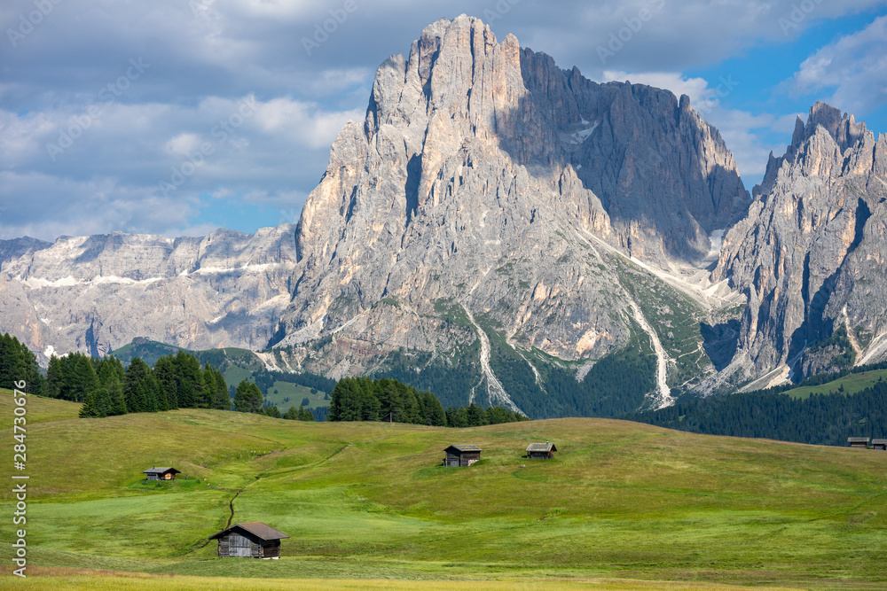 décors montagnard dans les alpes italiennes avec des chalets dans un grand champ fauché