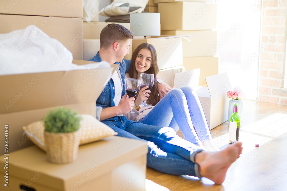 Young couple sitting on the floor of new house around cardboard boxes, celebrating drinking a glass of wine and smiling happy for new apartment Young couple sitting on the floor of new house around cardboard boxes, celebrating drinking a glass of wine and smiling happy for new apartment