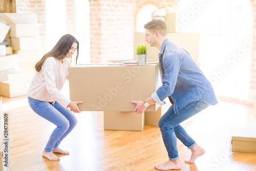 Beautiful young couple smiling in love holding a big cardboard box, happy for moving to a new home