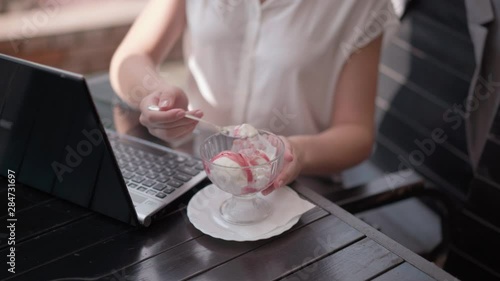 young business woman eating ice cream in a street cafe. she works with a laptop and talking on the phone.