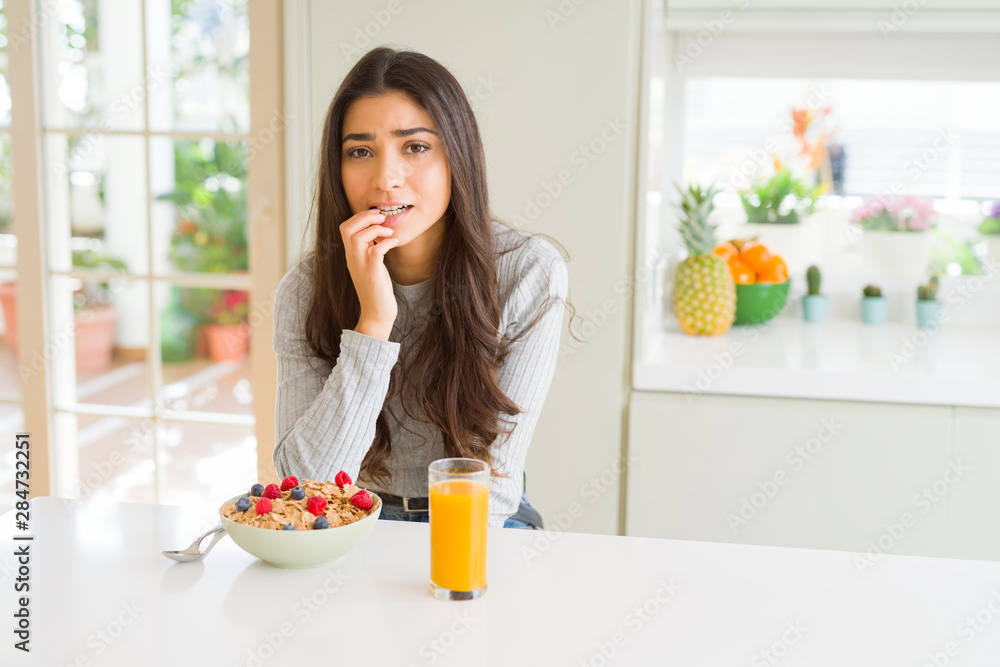 Young woman eating healthy breakfast in the morning looking stressed and nervous with hands on mouth biting nails. Anxiety problem. Young woman eating healthy breakfast in the morning looking stressed and nervous with hands on mouth biting nails. Anxiety problem.