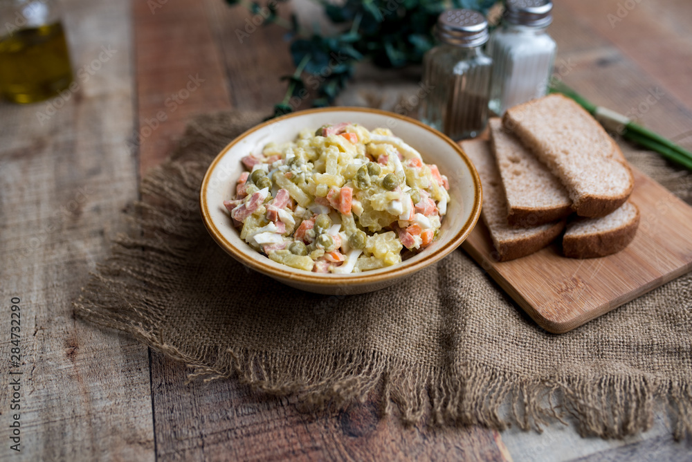 Bowl of traditional Russian salad called Olivie, Russian New Year or Christmas salad on wooden background. Salad from cooked vegetables. Potato salad. Bowl of traditional Russian salad called Olivie, Russian New Year or Christmas salad on wooden background. Salad from cooked vegetables. Potato salad.