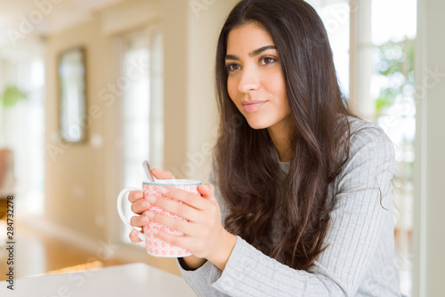 Beautiful young girl drinking a cup of coffee at home and smiling
