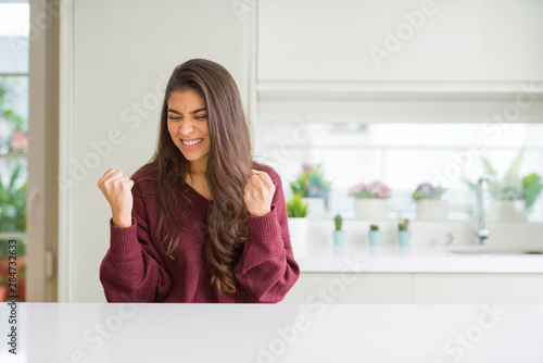 Young beautiful woman at home very happy and excited doing winner gesture with arms raised  smiling and screaming for success. Celebration concept.