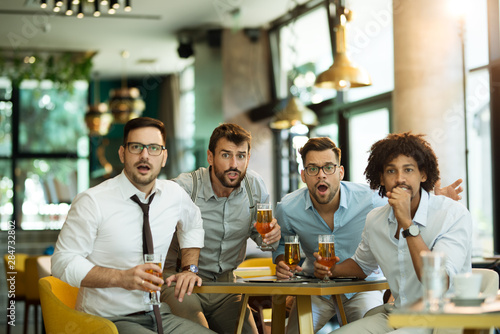 Four male friends are watching game drinking beer at the pub.