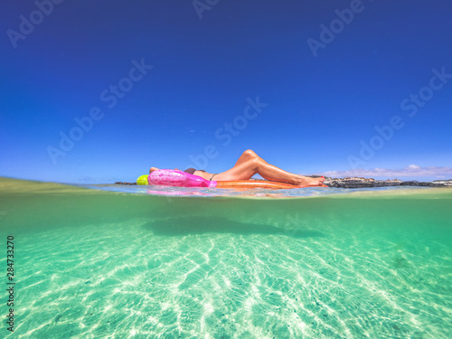 Girl sunbathing on an inflatable mattress floating on blue tropical water. Beautiful woman lying on a mat relaxing during exotic heavenly vacation. Shark view. Holiday, relax, travel summer concept