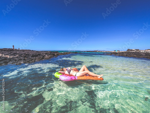 Girl sunbathing on an inflatable mattress shaped like ice cream cone floating on tropical water. Beautiful woman lying on a mat relaxing during exotic heavenly vacation. Holiday relax travel concept