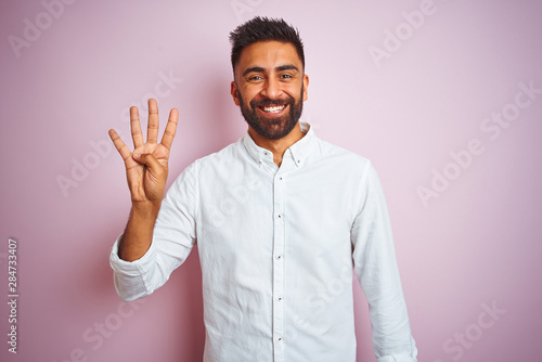 Valokuvatapetti Young indian businessman wearing elegant shirt standing over isolated pink background showing and pointing up with fingers number four while smiling confident and happy
