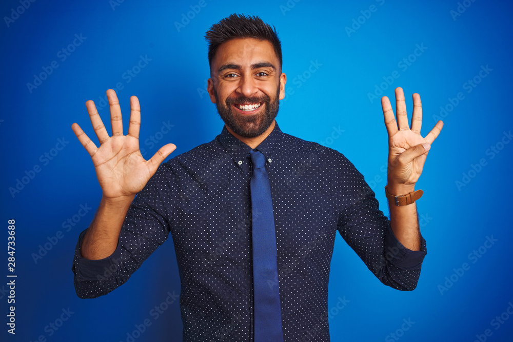 Young indian businessman wearing elegant shirt and tie standing over isolated blue background showing and pointing up with fingers number nine while smiling confident and happy. Young indian businessman wearing elegant shirt and tie standing over isolated blue background showing and pointing up with fingers number nine while smiling confident and happy.
