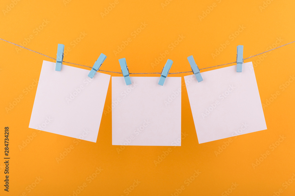 white sheets of notepad for notes and reminders, fastened with decorative blue clothespins, hang on a rope on an orange background white sheets of notepad for notes and reminders, fastened with decorative blue clothespins, hang on a rope on an orange background