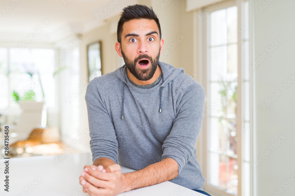 Handsome hispanic man wearing casual sweatshirt at home afraid and shocked with surprise expression, fear and excited face.