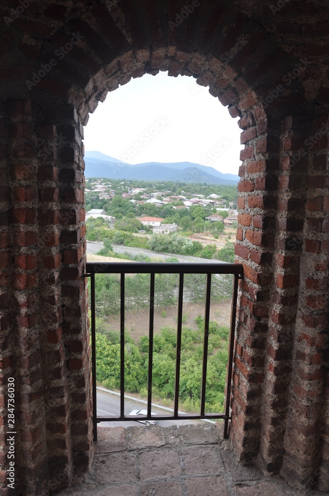 View of the sky, mountains and the valley through a brick window with a lattice in the tower