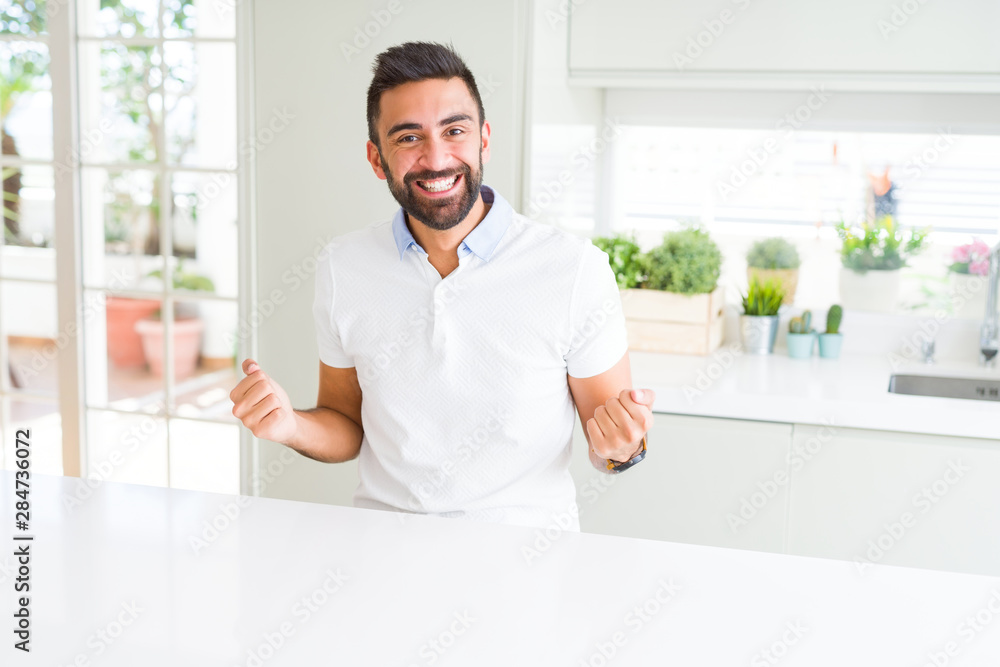 Handsome hispanic man casual white t-shirt at home celebrating surprised and amazed for success with arms raised and open eyes. Winner concept.
