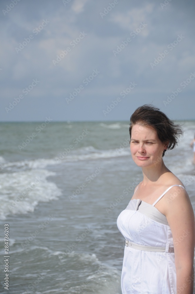 Close-up portrait of a girl in a white dress with short flying hair against the background of the sea Close-up portrait of a girl in a white dress with short flying hair against the background of the sea