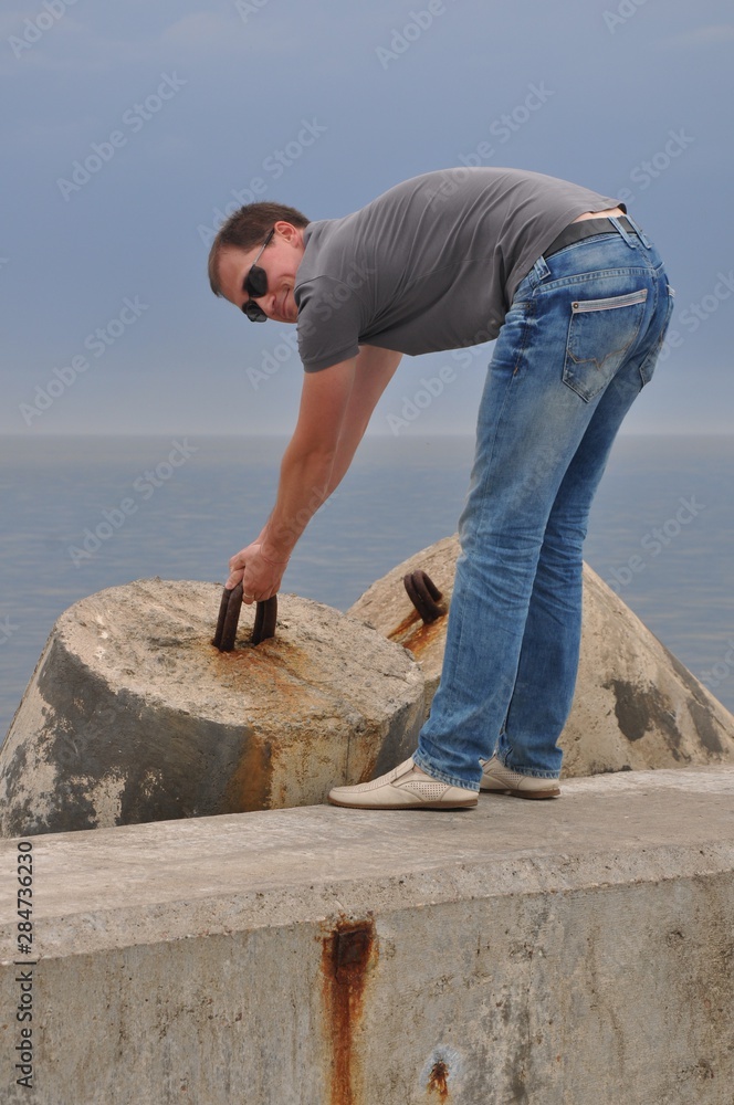 Young man in ordinary clothes trying to lift the breakwater by the bracket Young man in ordinary clothes trying to lift the breakwater by the bracket