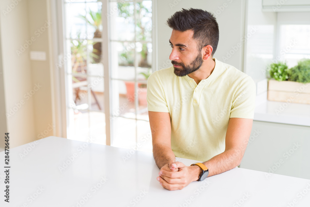 Handsome hispanic man casual yellow t-shirt at home looking to side, relax profile pose with natural face with confident smile.