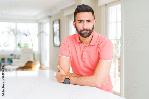Handsome hispanic man wearing casual t-shirt at home skeptic and nervous, disapproving expression on face with crossed arms. Negative person.