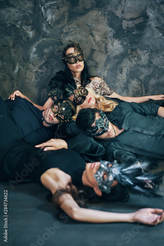 Group of friends in masquerade carnival mask sitting on floor relax after party photo