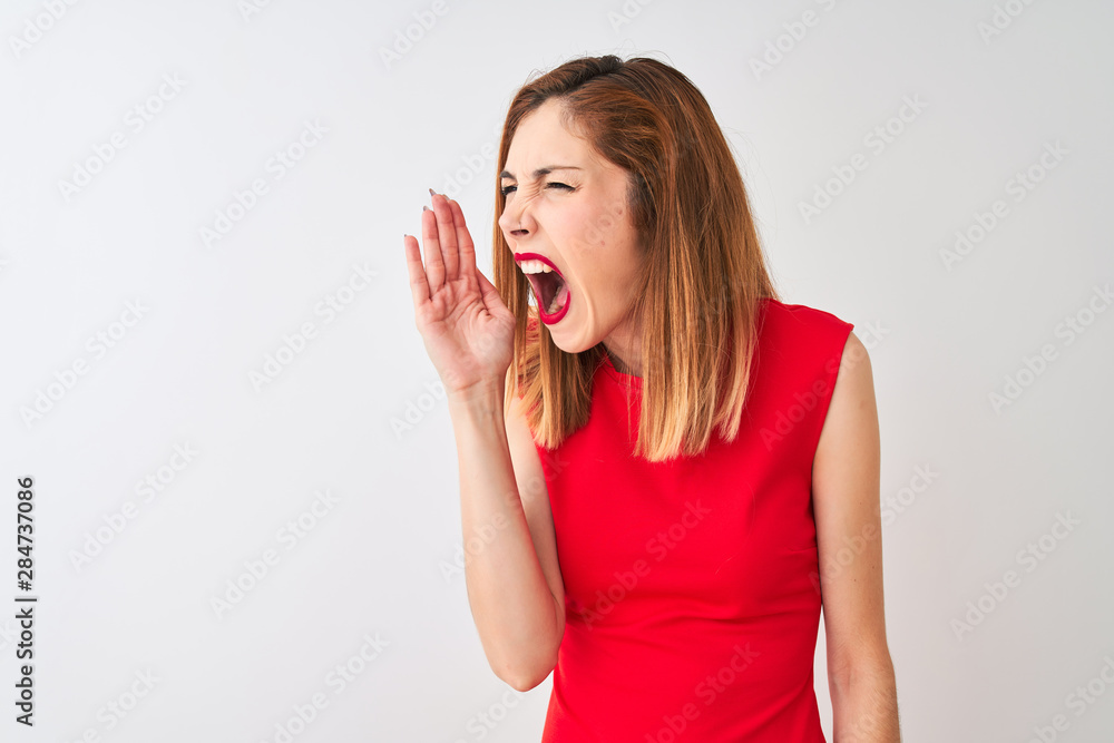Fototapeta premium Redhead businesswoman wearing elegant red dress standing over isolated white background shouting and screaming loud to side with hand on mouth. Communication concept.