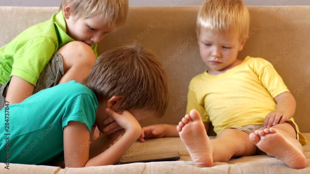 Happy calm children are playing with tablet. boys are happy together on vacation at their parents' house. Friendly joint preparation for school.
